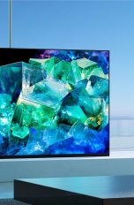 Ein Sony BRAVIA XR A95K steht auf einer TV-Bank vor einem großen Fenster.