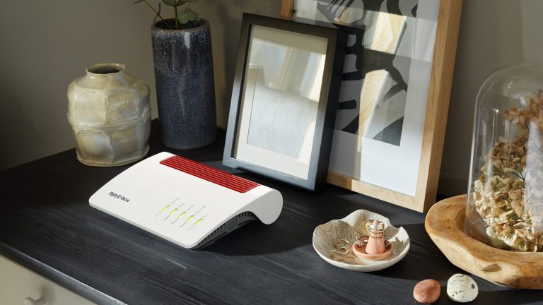 Fritzbox 7590 AX Eine Fritzbox 7590 AX steht mit zwei gerahmten Bildern und mehreren Vasen auf einer Kommode.