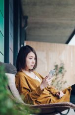 Eine Person sitzt in einem Stuhl auf einem Balkon und schaut auf ihr iPhone.
