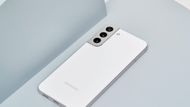 Samsung Galaxy S22 Plus Ein weißes Samsung Galaxy S22 liegt dekorativ auf einer grauen Unterlage.