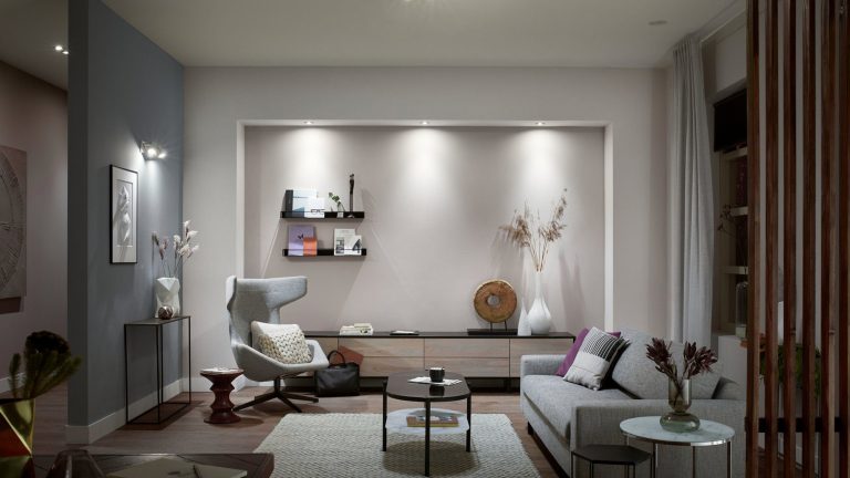 Philips Hue White Ambiance Blick in ein möbliertes Wohnzimmer. Von der Decke und den Wänden illuminieren “White Ambience”-Birnen von Philips Hue den Raum in einem tageslichtähnlichen Weiß.