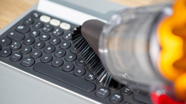 Tastatur reinigen Ein Handstaubsauger fährt über die Oberseite einer Tastatur.
