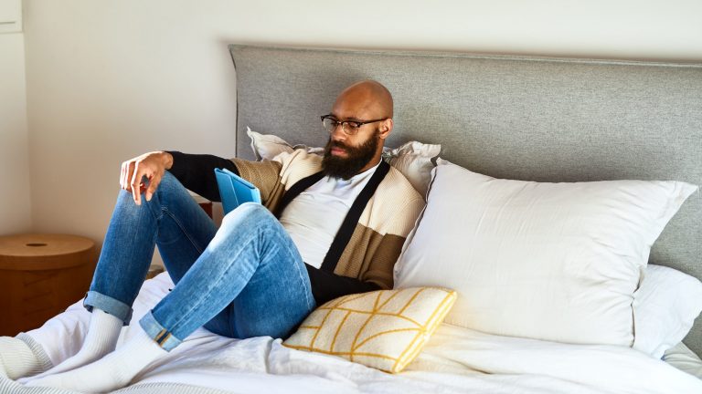 Eine Person sitzt mit ihrem Tablet im Bett und liest.