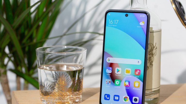 Xiaomi Redmi 10 Ein Redmi 10 lehnt auf einem Tisch stehend an einer Flasche.