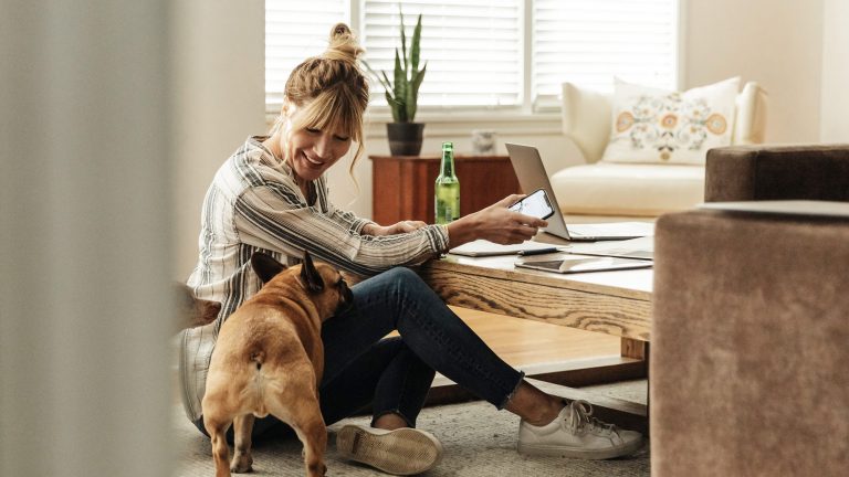 Apple Universal Control Eine Person sitzt auf dem Boden vor ihrem Wohnzimmertisch, darauf steht ein MacBook, in der Hand hält sie ein iPad, neben der Person steht ein Hund.