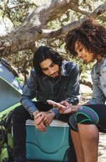 Zwei Personen sitzen im Freien vor einem Campingzelt und schauen gemeinsam auf ein Smartphone.