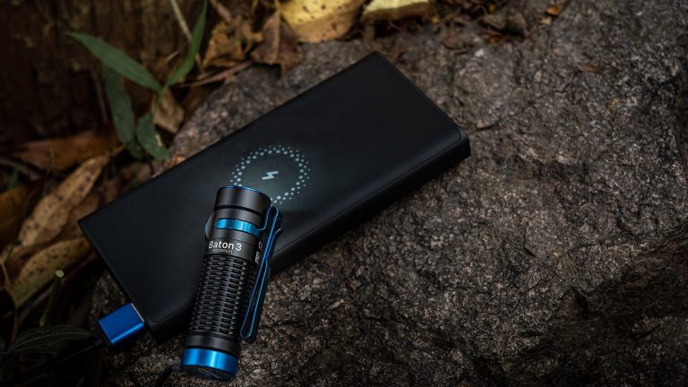 Taschenlampe Olight Baton 3 Eine Outdoor-Taschenlampe liegt zusammen mit einer Powerbank auf einem großen Stein im Freien.