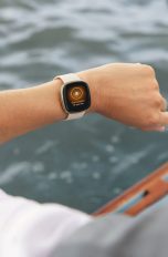 Eine Person sitzt in einem Boot und blickt auf ihren linken Arm, an dem sich ein Fitness-Tracker befindet.