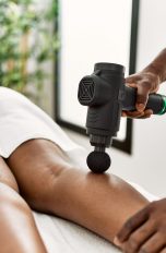 Eine Person liegt auf einer Massageliege und wird mit einer Massagepistole an der Wade behandelt.