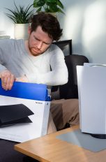 Eine Person sitzt auf einem Sofa vor einer PS5 und zieht schwarze Seitenteile für die Konsole aus einem Karton.
