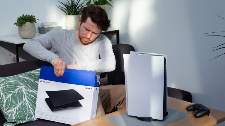 Eine Person sitzt auf einem Sofa vor einer PS5 und zieht schwarze Seitenteile für die Konsole aus einem Karton.