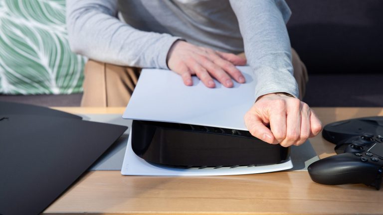 PlayStation 5: So wechselst du die Seitenteile Eine Person zieht am oberen Ende der Abdeckung einer vor ihr liegenden PS5.