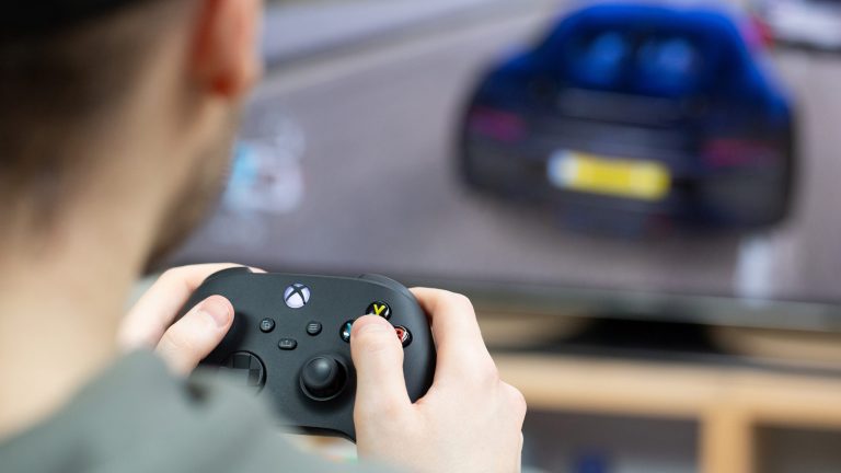 Eine Person sitzt mit einem Controller vor einem Bildschirm und spielt Autorennen.