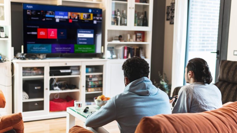 Auf einem Sofa sitzen zwei Personen und schauen auf den Bildschirm ihres Smart-TVs.