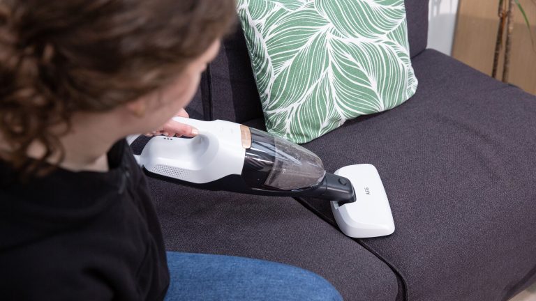 AEG Akku-Stielstaubsauger QX7-1-ULTAL Eine Person sitzt auf einem Sofa und saugt mit einem Handstaubsauger.