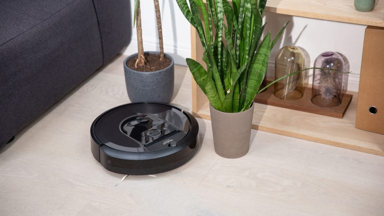 iRobot Roomba i7 Ein Saugroboter saugt den Boden, neben ihm stehen zwei Pflanzen.