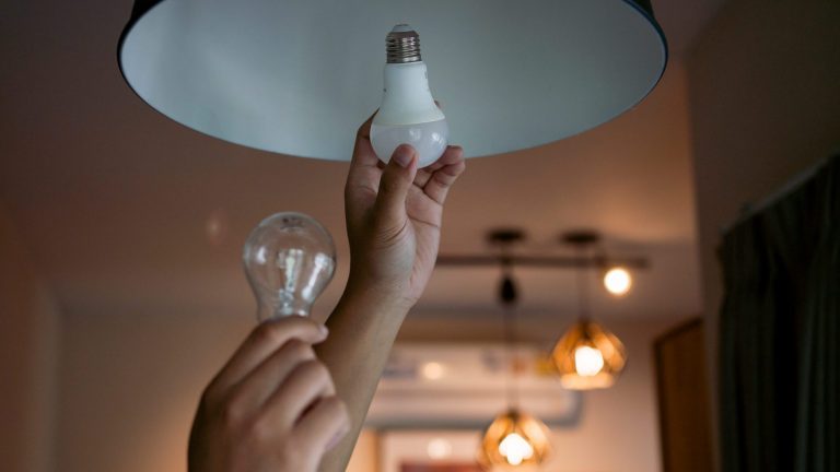 LED Lampe Eine Person entfernt eine klassische Glühlampe aus einer Hängelampe und tauscht sie gegen eine LED-Lampe.