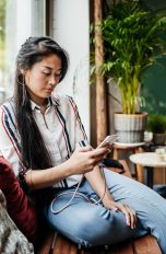 Eine Person sitzt auf einer Holzbank in einem Café und schaut auf ihr Smartphone.