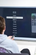 Eine Person sitzt vor einem Fernseher, an den ein Apple TV angeschlossen ist und stellt die Sprache für das System ein.