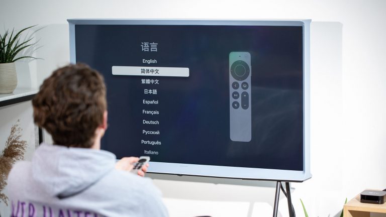 Eine Person sitzt vor einem Fernseher, an den ein Apple TV angeschlossen ist und stellt die Sprache für das System ein.