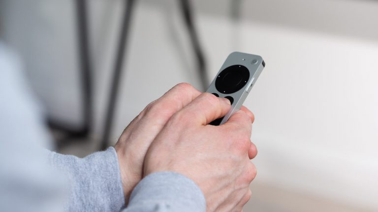 Apple TV ausschalten und neu starten Eine Person hält eine Fernbedienung des Apple TV in der Hand und drückt dabei auf zwei Tasten.