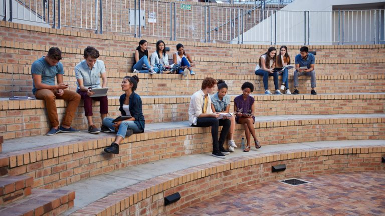 Mehrere Studierende sitzen auf ihrem Campus in Gruppen zusammen.