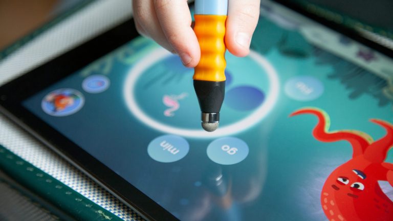 Der Edurino-Stift, geführt von einer Kinderhand, tippt auf einem Tablet auf verschiedene Wörter.