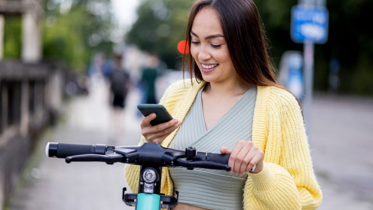 E-Scooter in Deutschland per App mieten Eine Person steht mit ihrem Smartphone an einem E-Scooter, um ihn auszuleihen.