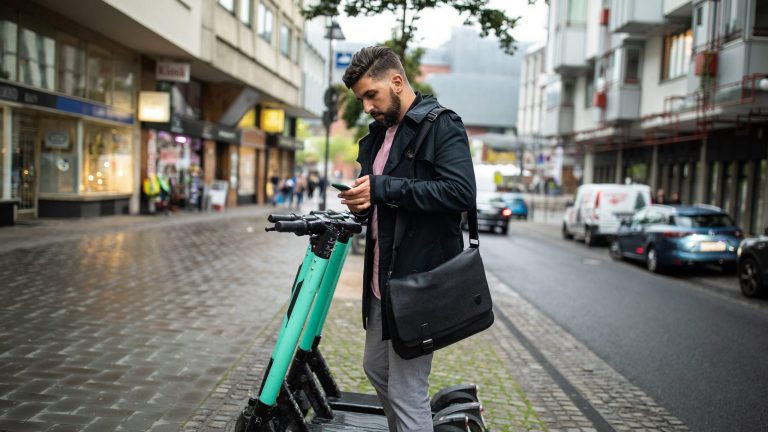E-Scooter in Deutschland per App mieten Eine Person steht mit dem Smartphone in der Hand vor einem E-Scooter.