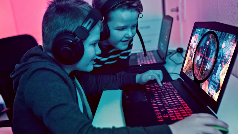 Mobil zocken, 6 Gaming-Notebooks mit ordentlich Power Zwei Kinder sitzen vor einem Gaming-Notebook und spielen. Im Hintergrund steht ein weiteres Gaming-Notebook.