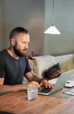 Eine Person sitzt mit ihrem Laptop am Tisch.