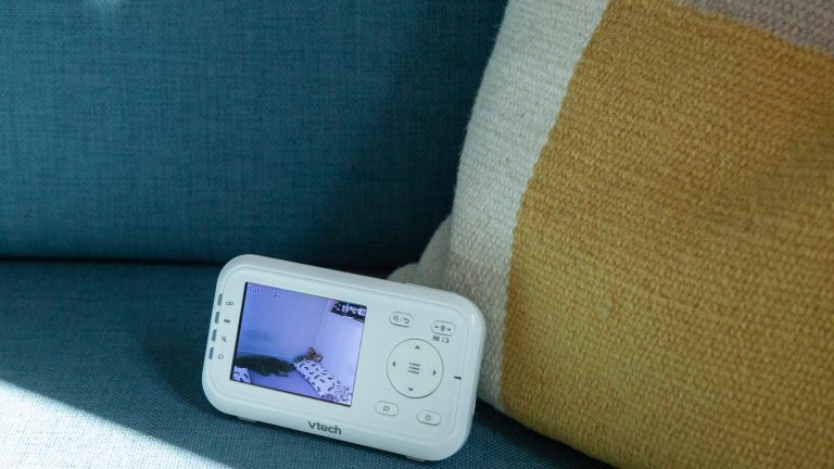 Vtech Video-Babyphone VM 3255 Das Elternteil des Babyphon VM 3255 von Vtech steht eingeschaltet auf einem Sofa. Auf dem Display ist der Blick in ein Kinderzimmer zu erkennen.