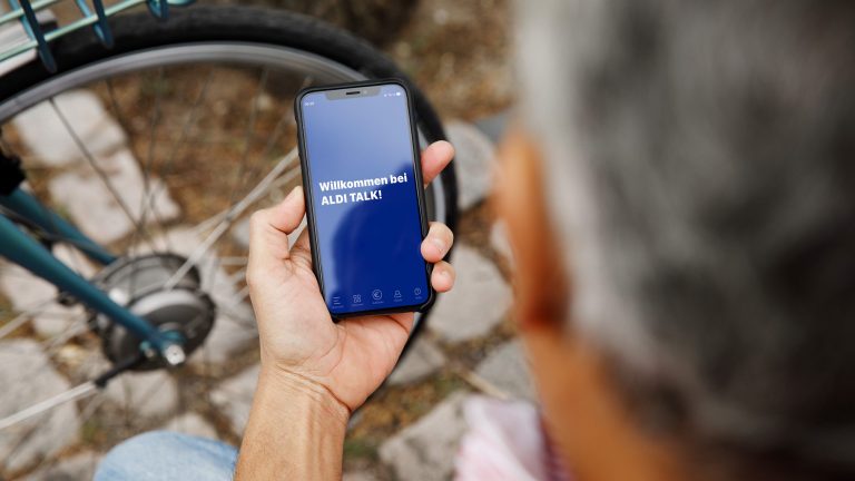 ALDI TALK-App funktioniert nicht Eine Person blickt sitzend auf ihr Smartphone, auf dem die Aldi-Talk-App startet.