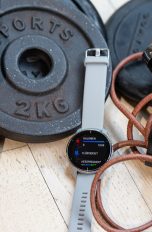 Auf einigen Hantelscheiben liegen drei Fitness-Tracker von Huawei, Xiaomi und Garmin.