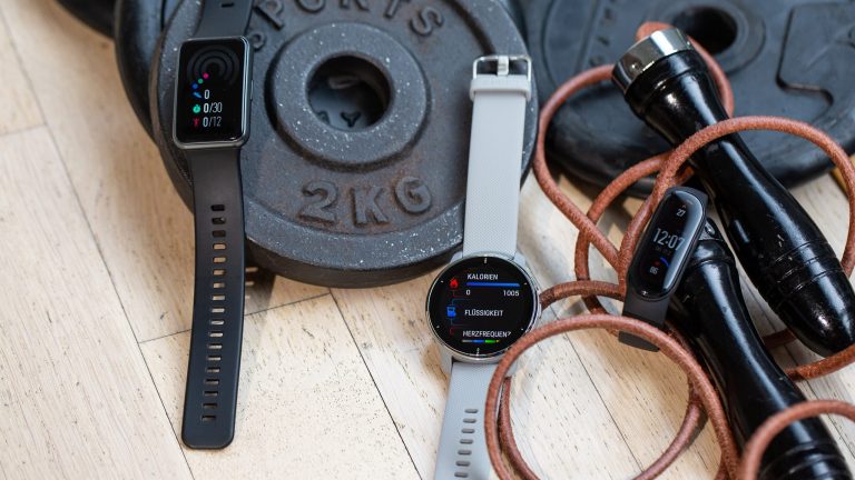 Auf einigen Hantelscheiben liegen drei Fitness-Tracker von Huawei, Xiaomi und Garmin.