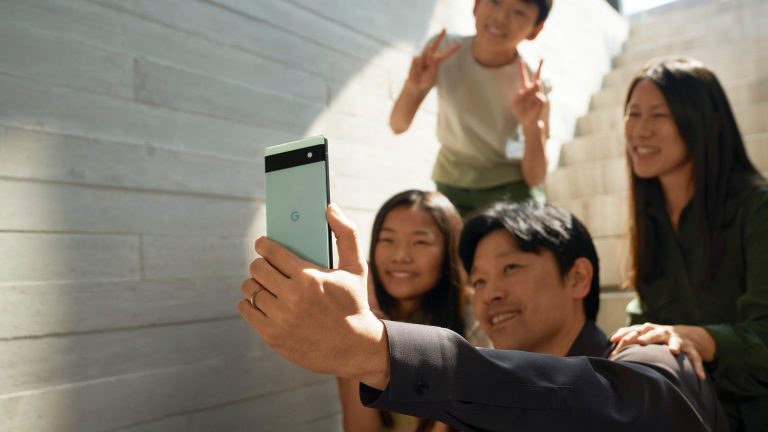 Google Pixel 6a Eine vierköpfige Familie sitzt und steht teilweise auf einer Treppe. Sie lächelt in die Frontkamera eines Google Pixel 6a.