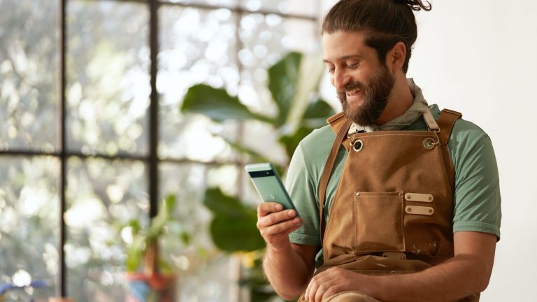 Google Pixel 6a Eine Person in Arbeitsschürze hält ein grünes Google Pixel 6a in der Hand und lächelt.