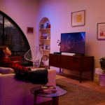 Zwei Personen sitzen auf einem Sofa vor einem Fernseher mit Soundbar.