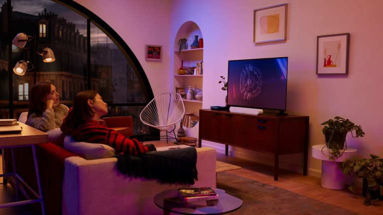Zwei Personen sitzen auf einem Sofa vor einem Fernseher mit Soundbar.