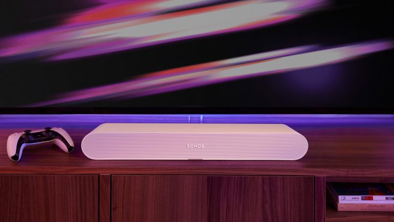 Sonos Ray Die Soundbar Sonos Ray steht vor einem Fernseher, neben Ihr liegt ein Playstation-Controller.