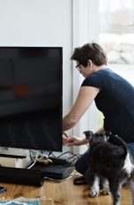 Eine Person kniet auf dem Boden neben ihrem Fernseher und arbeitet an der Verkabelung.