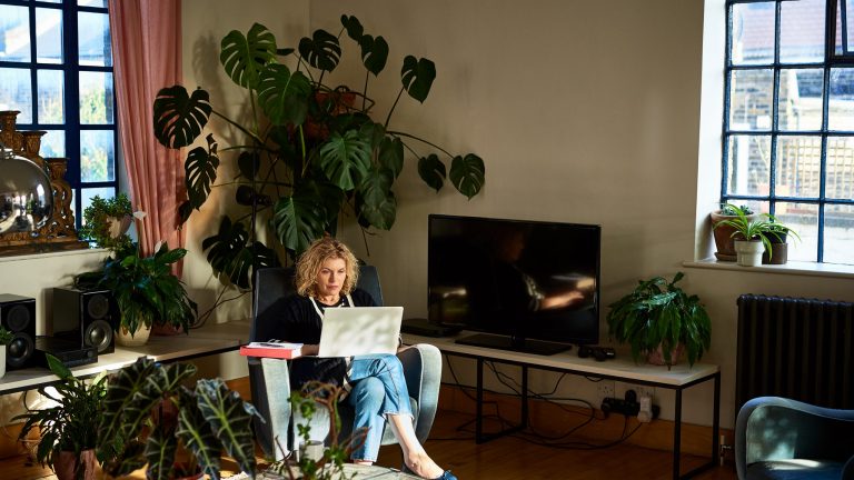 Eine Person sitzt im Wohnzimmer in einem Sessel, mit einem Laptop auf dem Schoß.