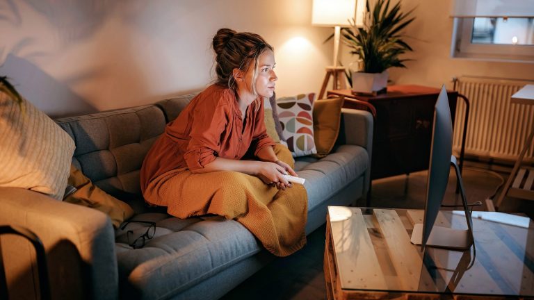 Audio- und Video-Streaming daheim Eine Person sitzt auf ihrem Sofa und schaut auf einen Bildschirm, der auf dem Tisch vor ihr steht.