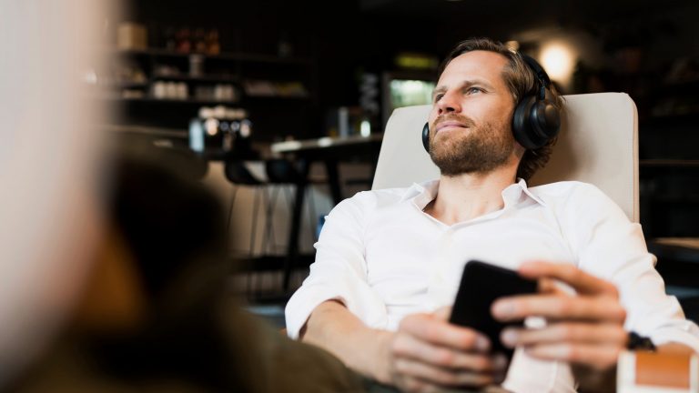 Audio- und Video-Streaming daheim Eine Person sitzt entspannt in einem Sessel, auf dem Kopf trägt sie einen Kopfhörer, in der Hand hält sie ein Smartphone.