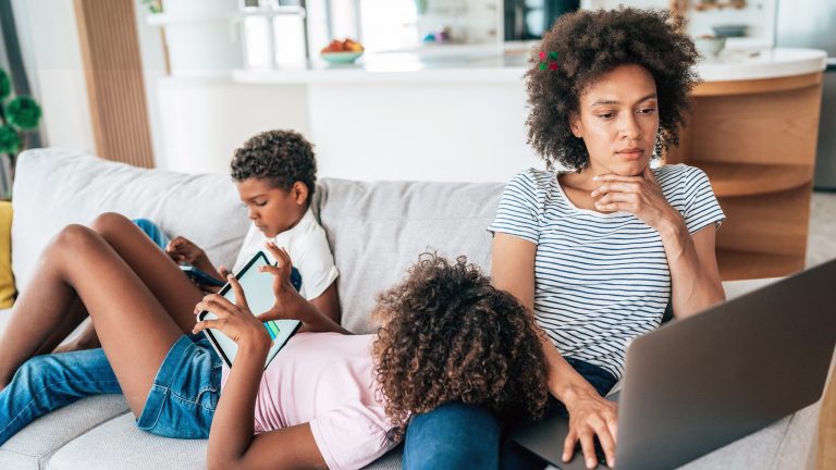 Audio- und Video-Streaming daheim Drei Personen sitzen und liegen auf einem Sofa, sie surfen auf Laptop, Tablet und Smartphone.
