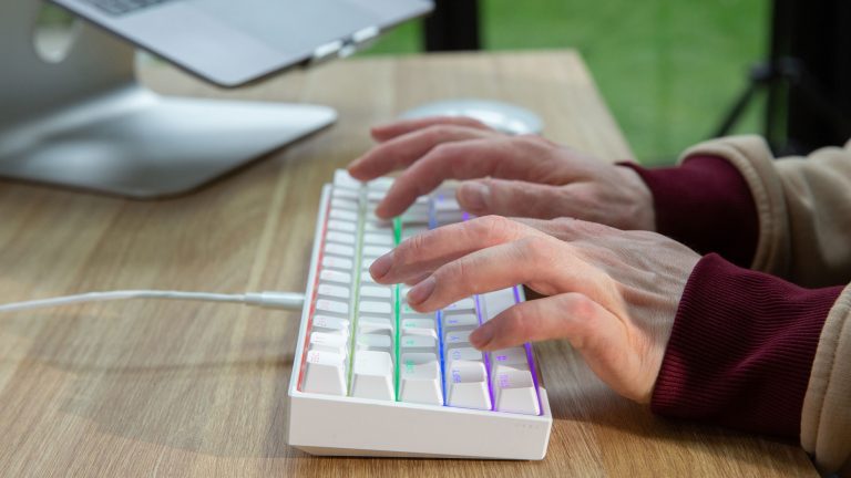 Corsair K65 RGB Mini Eine Person tippt auf einer bunt leuchtenden Corsair K65 Mini.