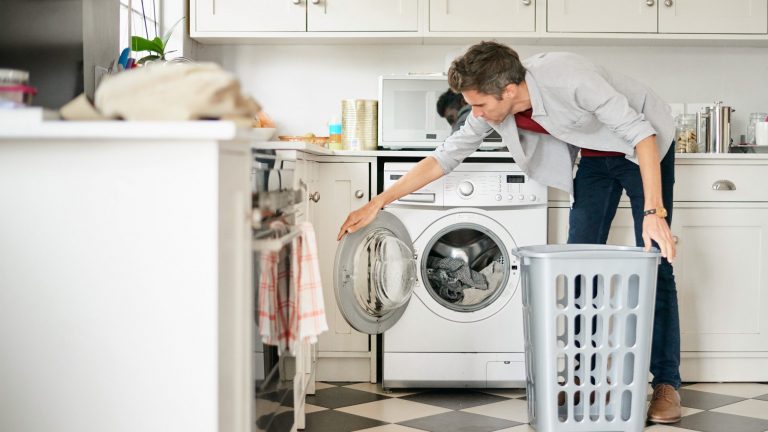 Energiesparen Eine Person steht mit einem Wäschekorb vor einer Waschmaschine.