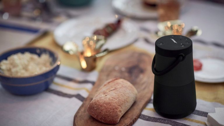 Ein Bose SoundLink Revolve+ II steht auf einem gedeckten Tisch neben einem Brötchen.