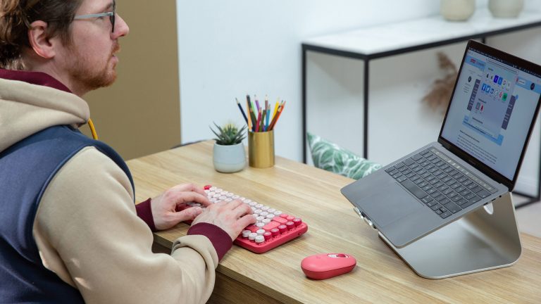 Logitech Pop Keys Eine Person tippt auf einer Logitech Pop Keys. Daneben liegen eine farblich passende Maus und ein MacBook Pro.