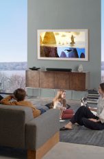 Zwei Eltern sitzen mit ihren beiden Kindern im Wohnzimmer vor einem Fernseher, der an der Wand hängt.